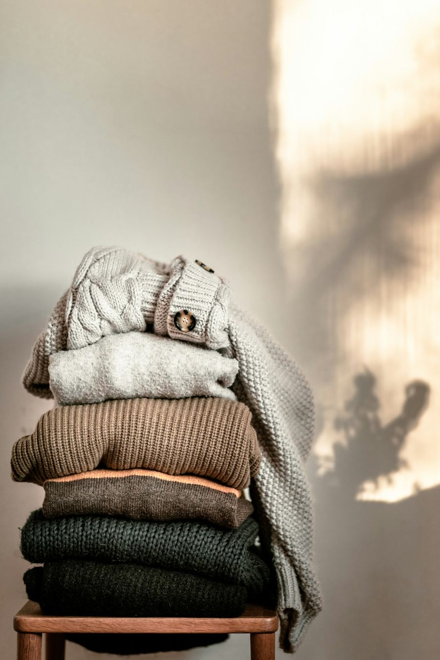 Folded knitwear stacked on a wooden chair in soft morning light
